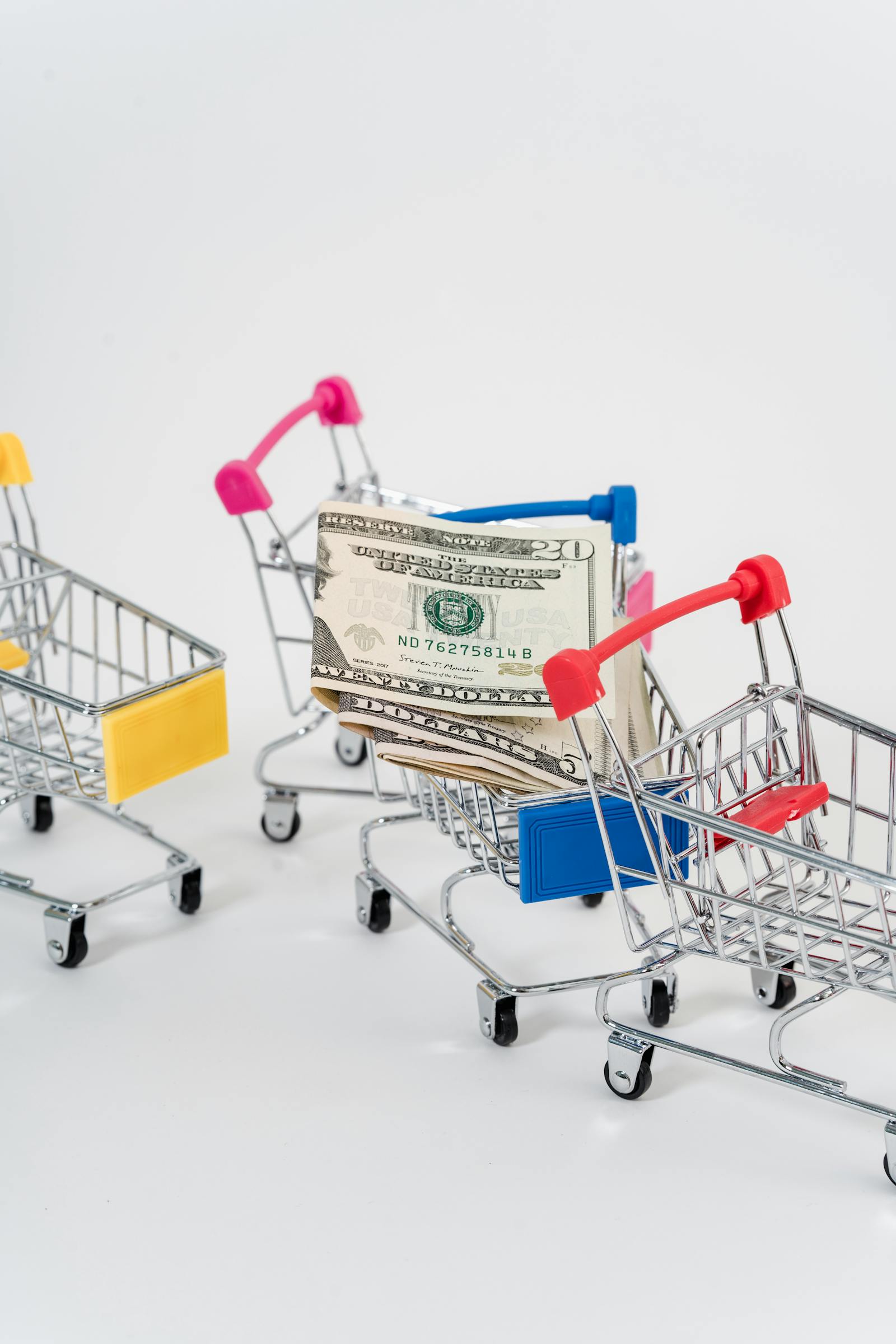 Close-up of US dollar bills next to miniature shopping carts on a flat surface