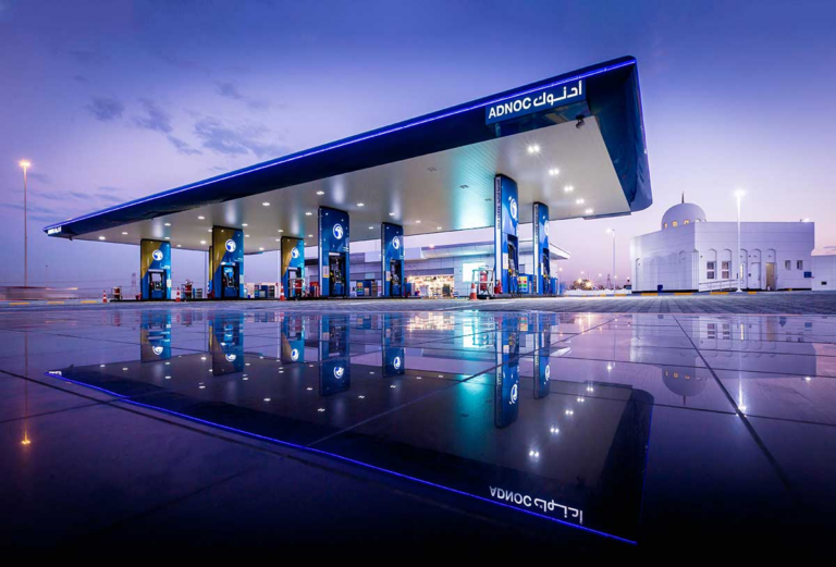 An ADNOC petrol station with its lit canopy and fuel pumps reflected on the forecourt, UAE
