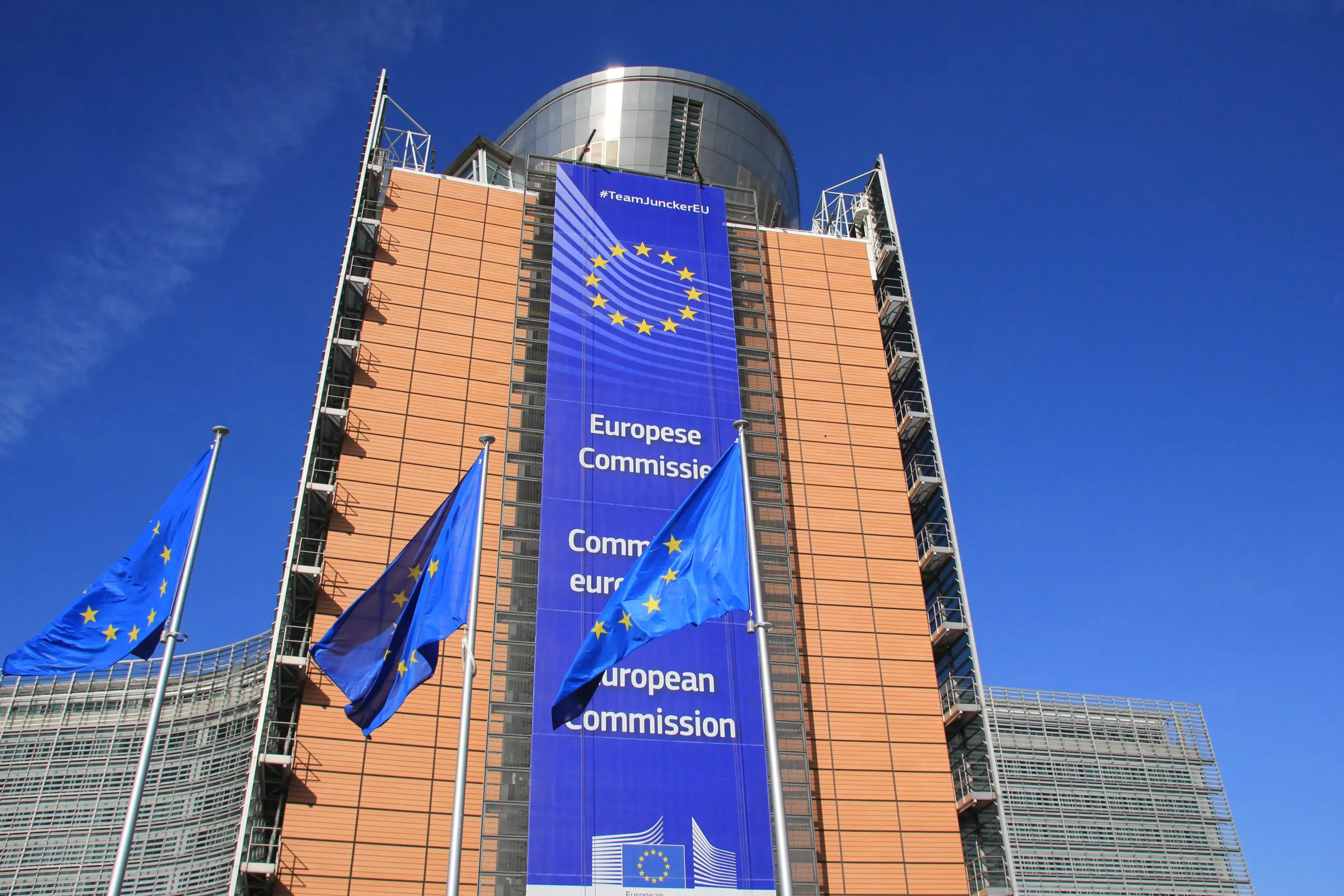 The Berlaymont building in Brussels, headquarters of the European Commission, with EU flags in front and a European Commission banner on its facade