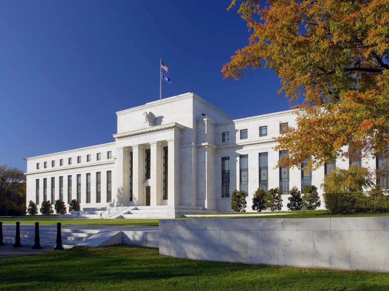 The Marriner S. Eccles Federal Reserve Board Building in Washington, DC, under a blue sky with autumn trees