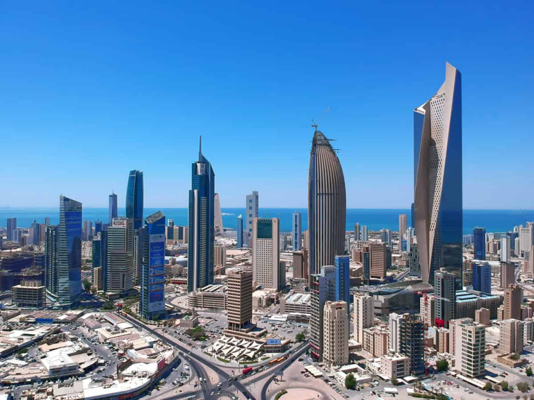 Aerial daytime view of the Kuwait City central business district, its high-rise commercial and financial towers rising above the surrounding streets with the Arabian Gulf beyond