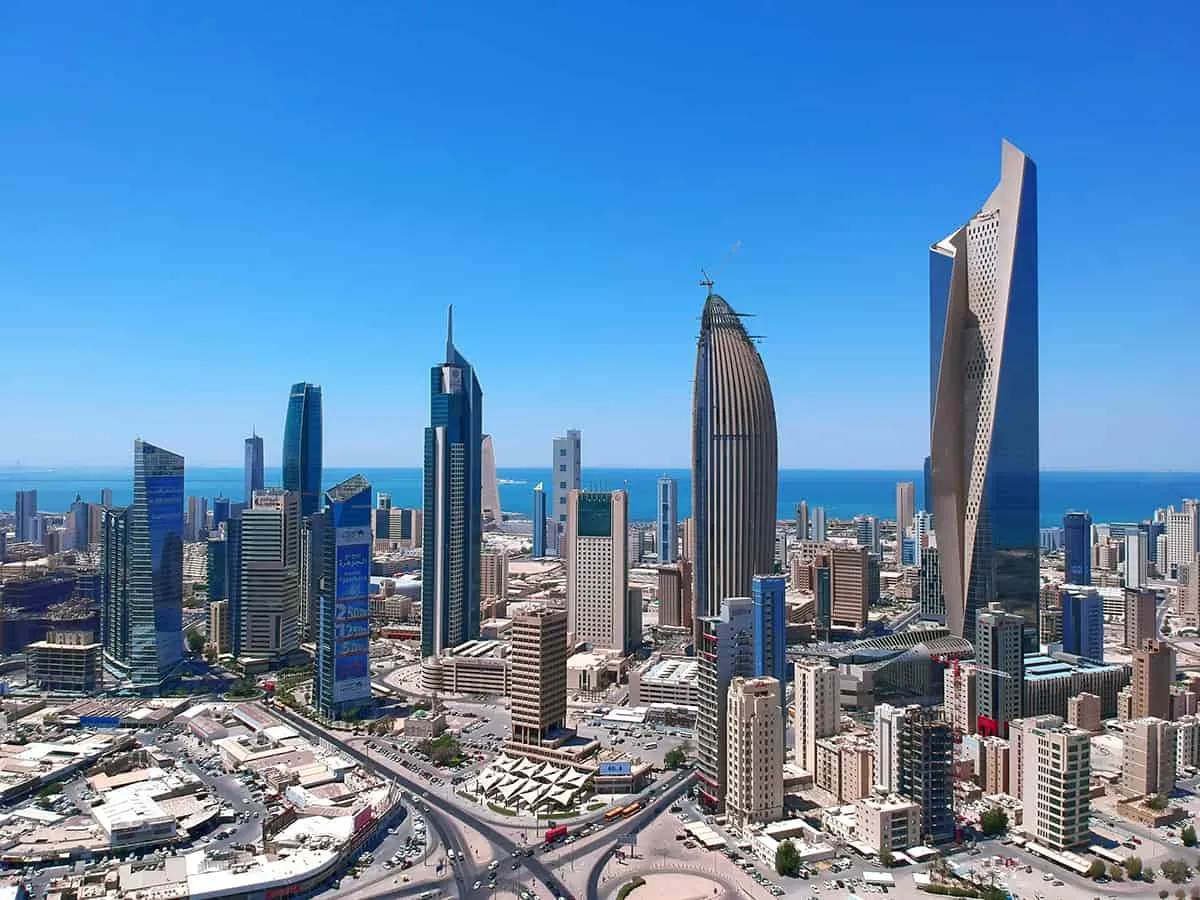 Aerial daytime view of the Kuwait City central business district, its high-rise commercial and financial towers rising above the surrounding streets with the Arabian Gulf beyond