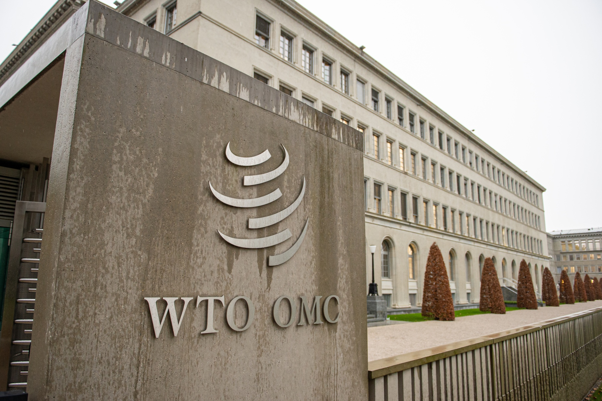 The World Trade Organization headquarters building in Geneva, Switzerland, with the entrance sign carrying the organisation emblem in the foreground