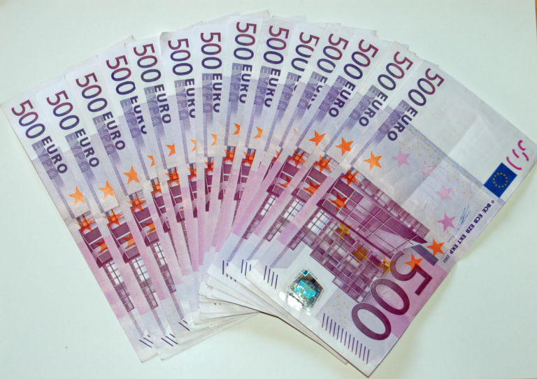 A fan of purple 500 euro banknotes spread across a white surface, showing the 500 EURO lettering, the EU flag and the hologram strip