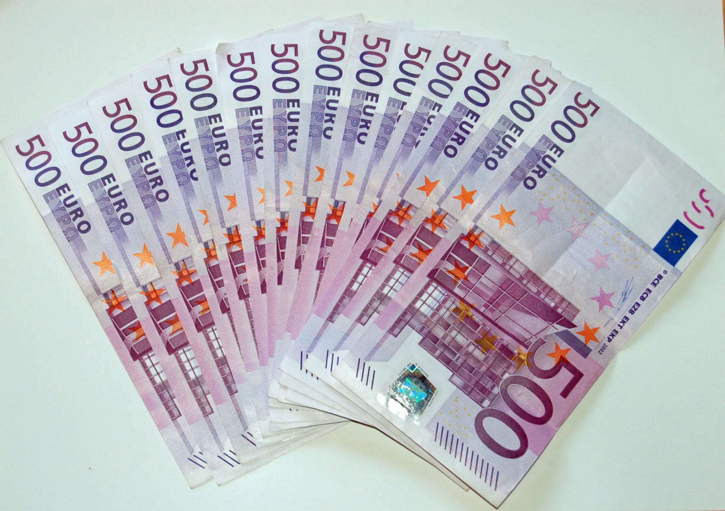 A fan of purple 500 euro banknotes spread across a white surface, showing the 500 EURO lettering, the EU flag and the hologram strip