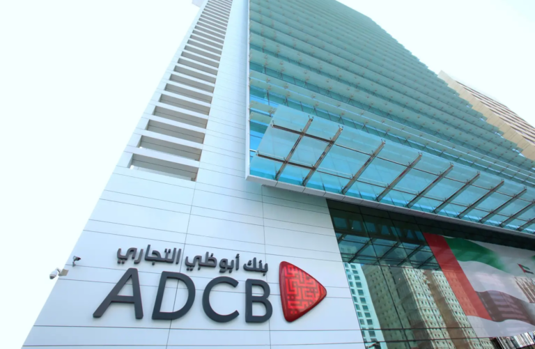 The ADCB logo and its Arabic and English names on the facade of a glass office tower, with a UAE flag