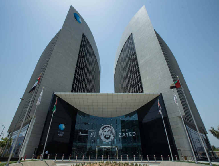 The twin curved towers of the Abu Dhabi Islamic Bank (ADIB) headquarters in Abu Dhabi, with the bank’s logo at the top and UAE flags at the entrance