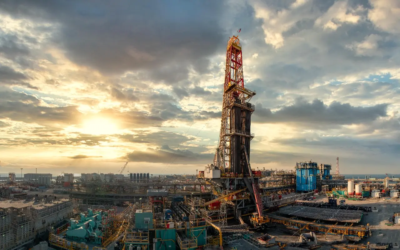 An ADNOC Drilling rig towering over production facilities at the Upper Zakum field, UAE, against a cloudy sky at sunset
