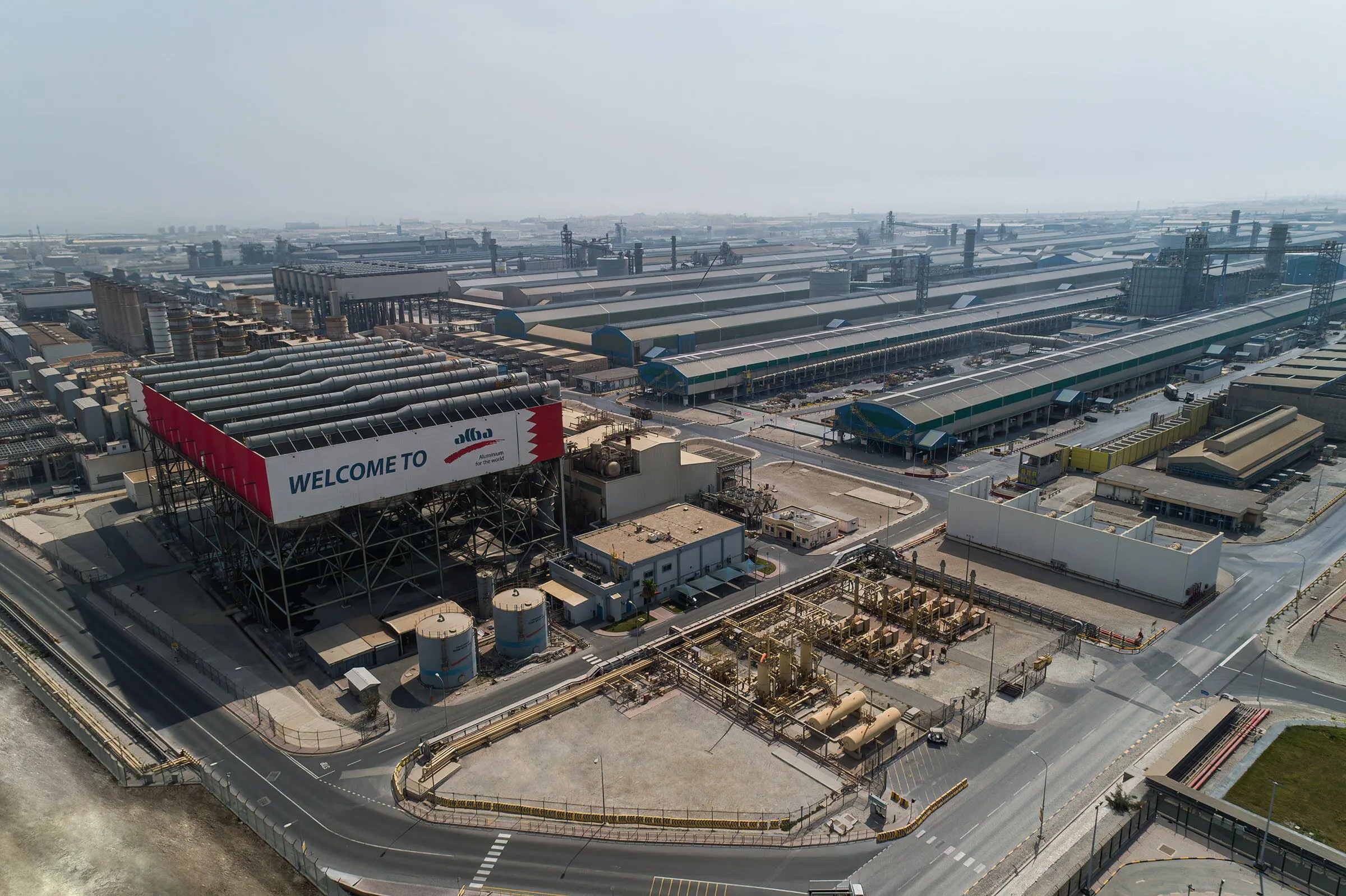 Aerial view of the Aluminium Bahrain (Alba) smelter complex, with long potline buildings, a Welcome to Alba sign and industrial roads