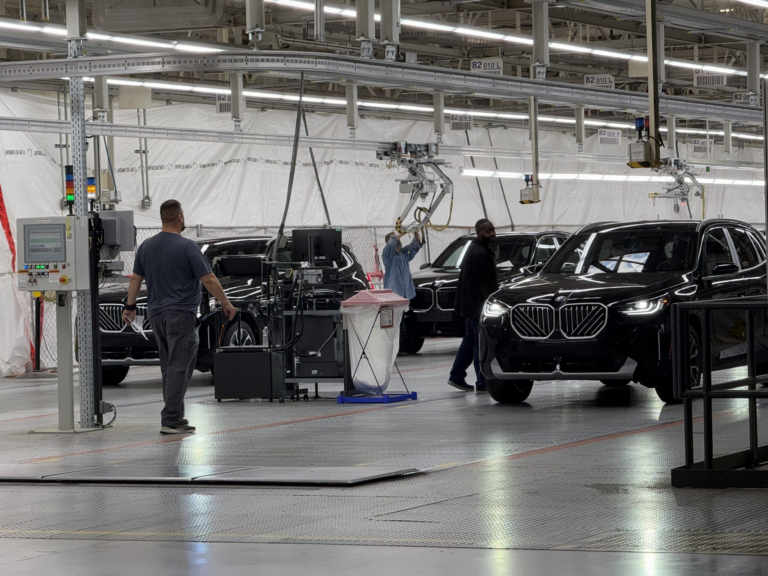 Workers beside black BMW SUVs on a vehicle assembly line in Egypt, under factory lights