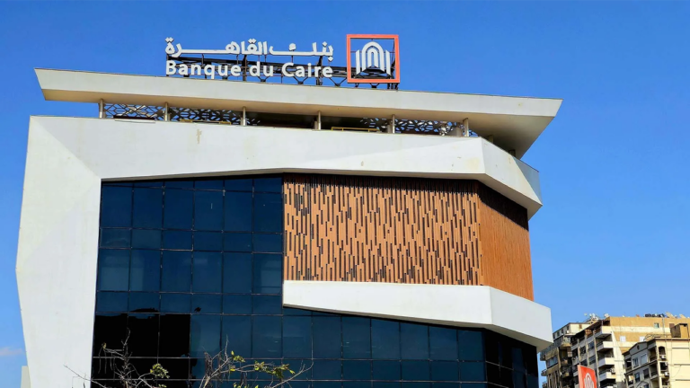 The modern glass and white facade of a Banque du Caire building in Egypt, with the bank name in Arabic and English and its logo on the roofline under a blue sky