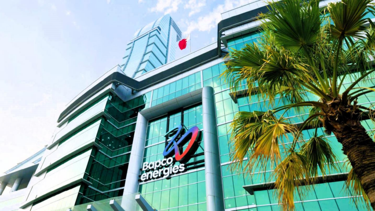 The Bapco Energies logo on a curved glass office building with a Bahrain flag on the roof and a palm tree in front
