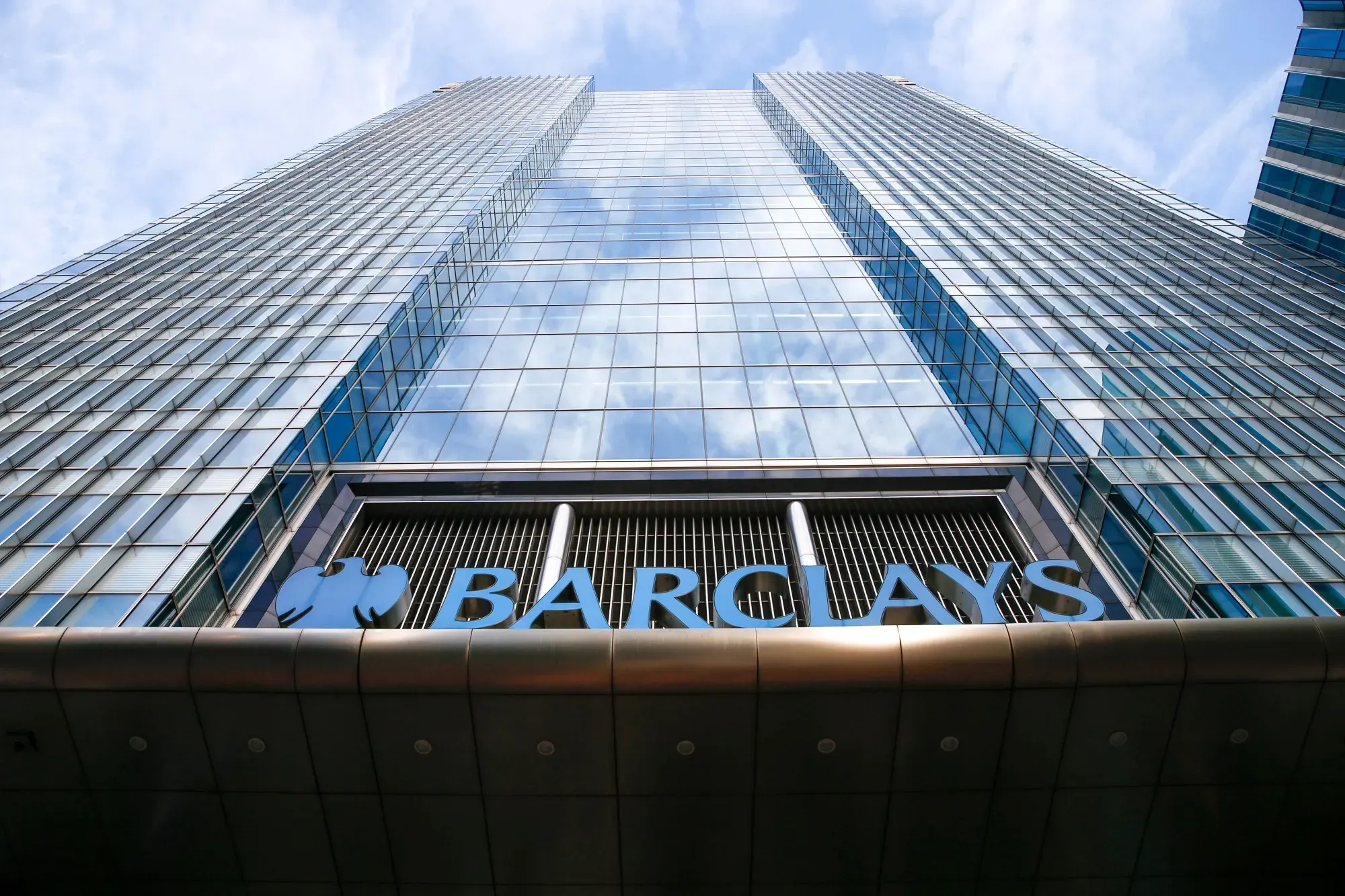 The Barclays name and eagle logo above the entrance of a glass office tower, seen from below