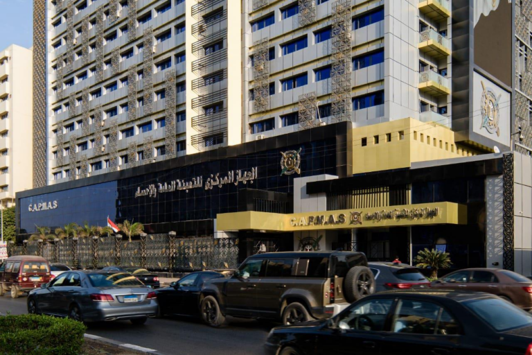 The building of Egypt's Central Agency for Public Mobilization and Statistics, with its name in Arabic, the CAPMAS lettering and emblem on the facade, an Egyptian flag and traffic in front