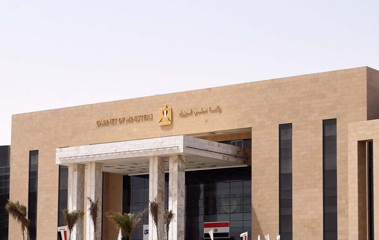 The stone facade of the Egyptian Cabinet of Ministers building, with its name in Arabic and English beside the national eagle emblem above a columned entrance and an Egyptian flag