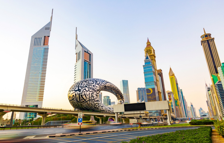 The Museum of the Future, its steel facade wrapped in Arabic calligraphy, beside the twin Emirates Towers and the high-rises of Sheikh Zayed Road in Dubai, with traffic on the highway in the foreground