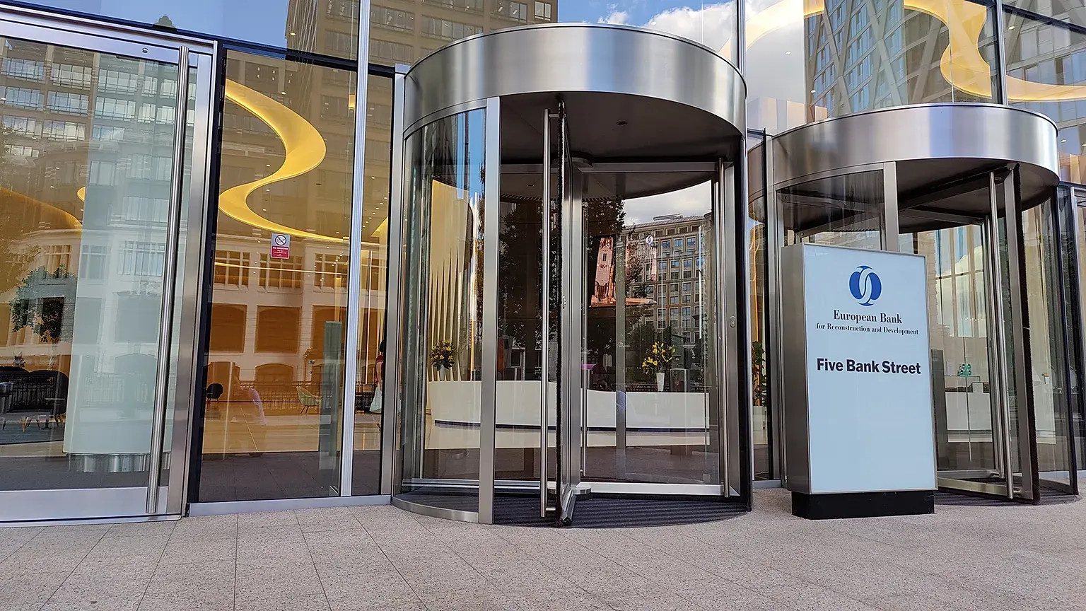 Revolving glass doors at the entrance of the European Bank for Reconstruction and Development, with a sign reading Five Bank Street