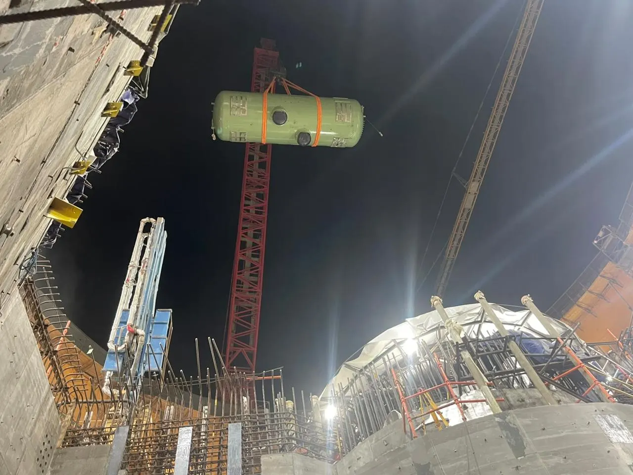 A steam generator lifted by a tower crane at night above the El Dabaa nuclear power plant construction site in Egypt