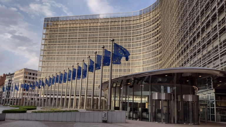The curved glass facade of the Berlaymont building in Brussels, headquarters of the European Commission, with a row of EU flags in front