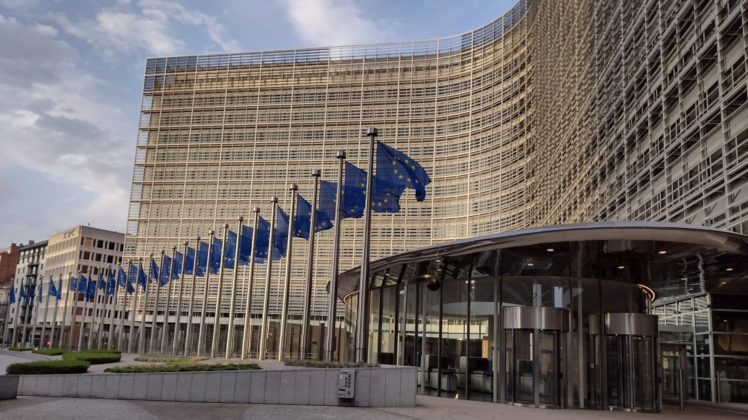 The curved glass facade of the Berlaymont building in Brussels, headquarters of the European Commission, with a row of EU flags in front