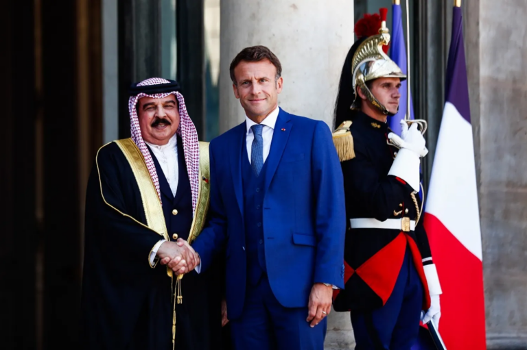 His Majesty King Hamad bin Isa Al Khalifa and French President Emmanuel Macron shake hands on the steps of the Élysée Palace in Paris, with a Republican Guard and the French flag