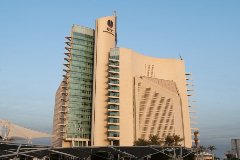 The Kuwait Petroleum Corporation headquarters tower in Kuwait, a stone and glass building with the KPC emblem near the top, under a clear sky