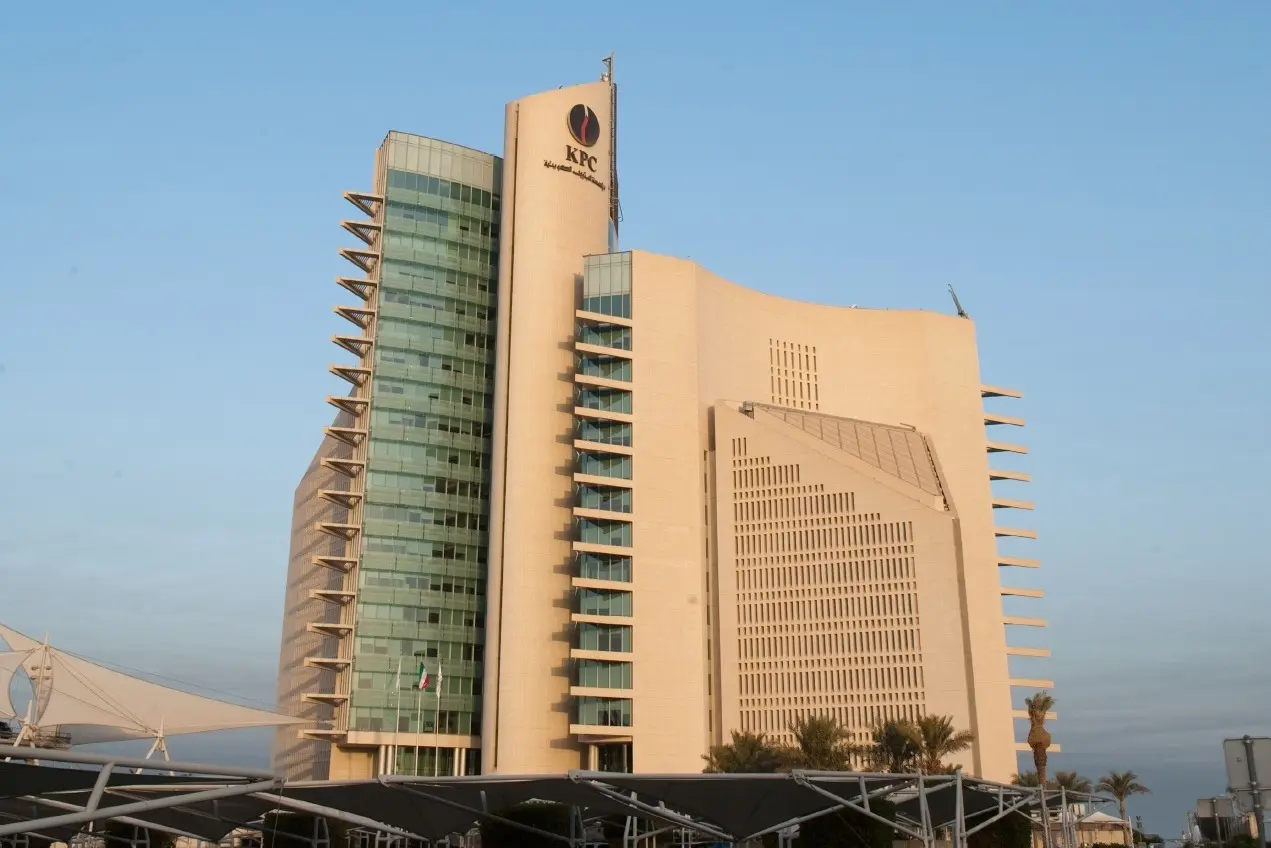 The Kuwait Petroleum Corporation headquarters tower in Kuwait, a stone and glass building with the KPC emblem near the top, under a clear sky