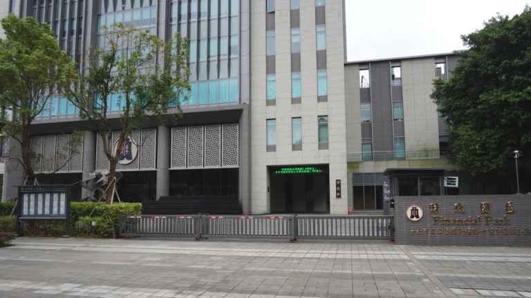 Main gate of the Ministry of Finance park in Taiwan, with a Financial Park sign beside a sliding gate in front of office buildings.