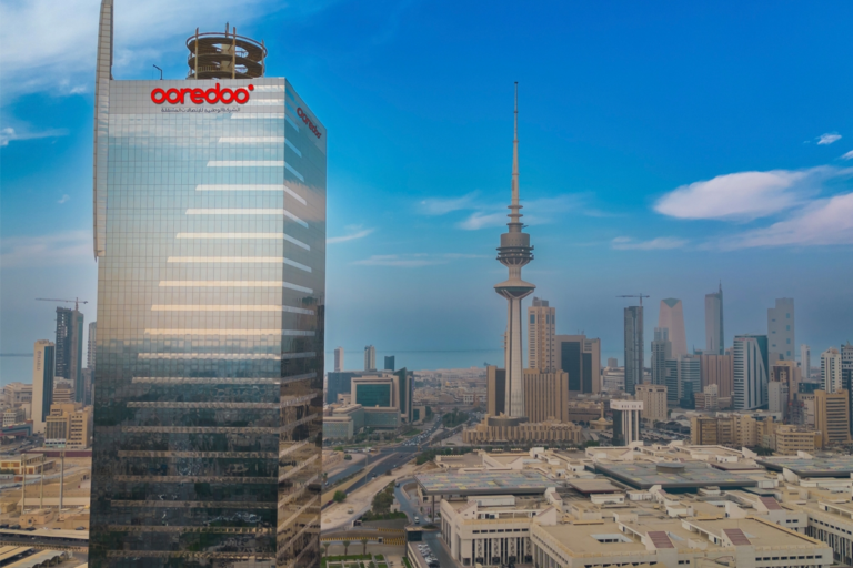 A glass tower bearing the Ooredoo logo beside the Kuwait City skyline and Liberation Tower