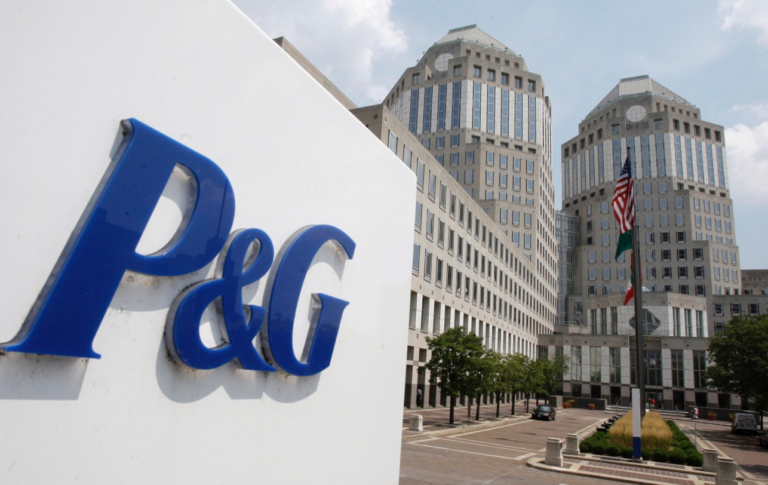 A blue P&G logo sign in front of the company's twin-towered headquarters, with flags on a flagpole