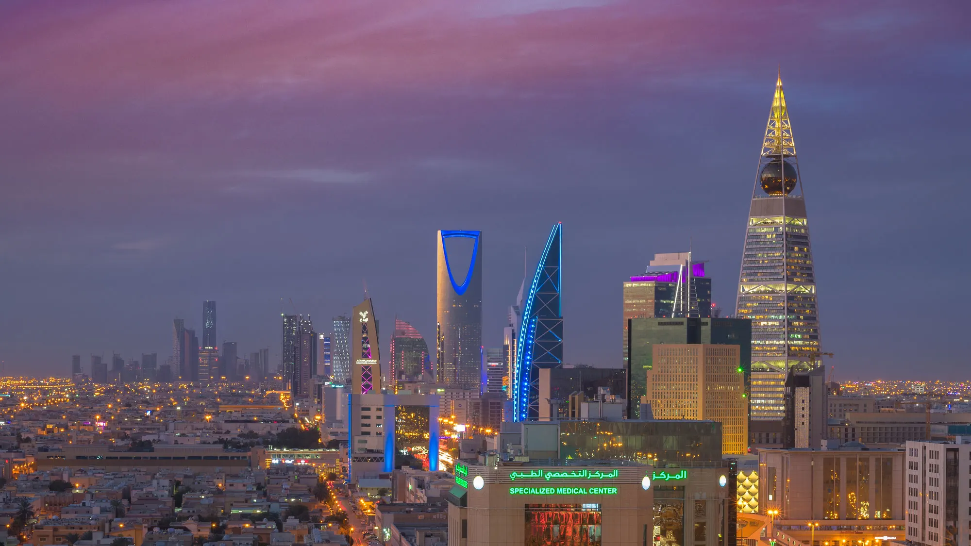 The Riyadh skyline at dusk, with Kingdom Centre and Al Faisaliah Tower lit against a purple sky, Saudi Arabia