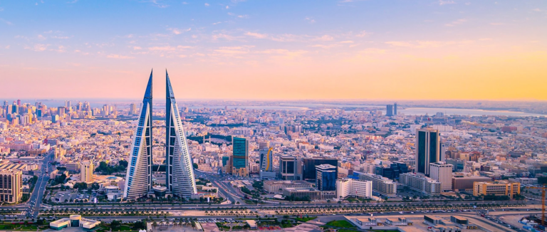 Aerial view of the Bahrain World Trade Center's twin sail-shaped towers and the Manama skyline under a pastel sky