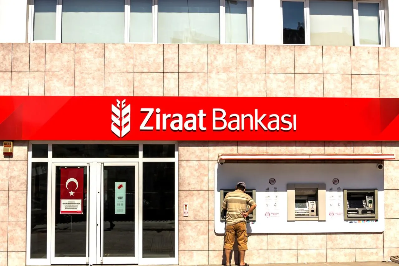The front of a Ziraat Bankası branch in Türkiye, with the bank name in white on a red sign above the entrance and a customer using a cash machine