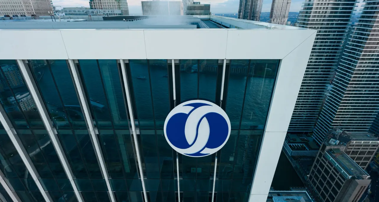 The EBRD logo on the glass and white corner of its headquarters tower in London, with neighbouring towers and the river behind