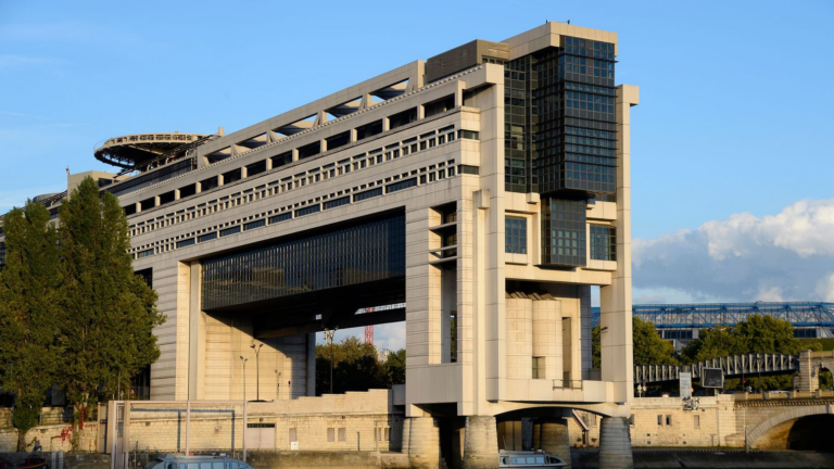 The Ministry of Economy and Finance building at Bercy in Paris, spanning the bank of the Seine on its concrete piers under a blue sky