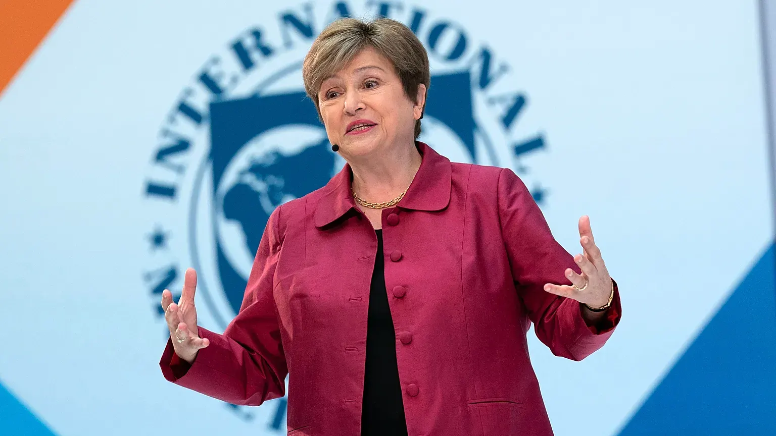 IMF Managing Director Kristalina Georgieva speaking on stage in a red jacket in front of the International Monetary Fund emblem