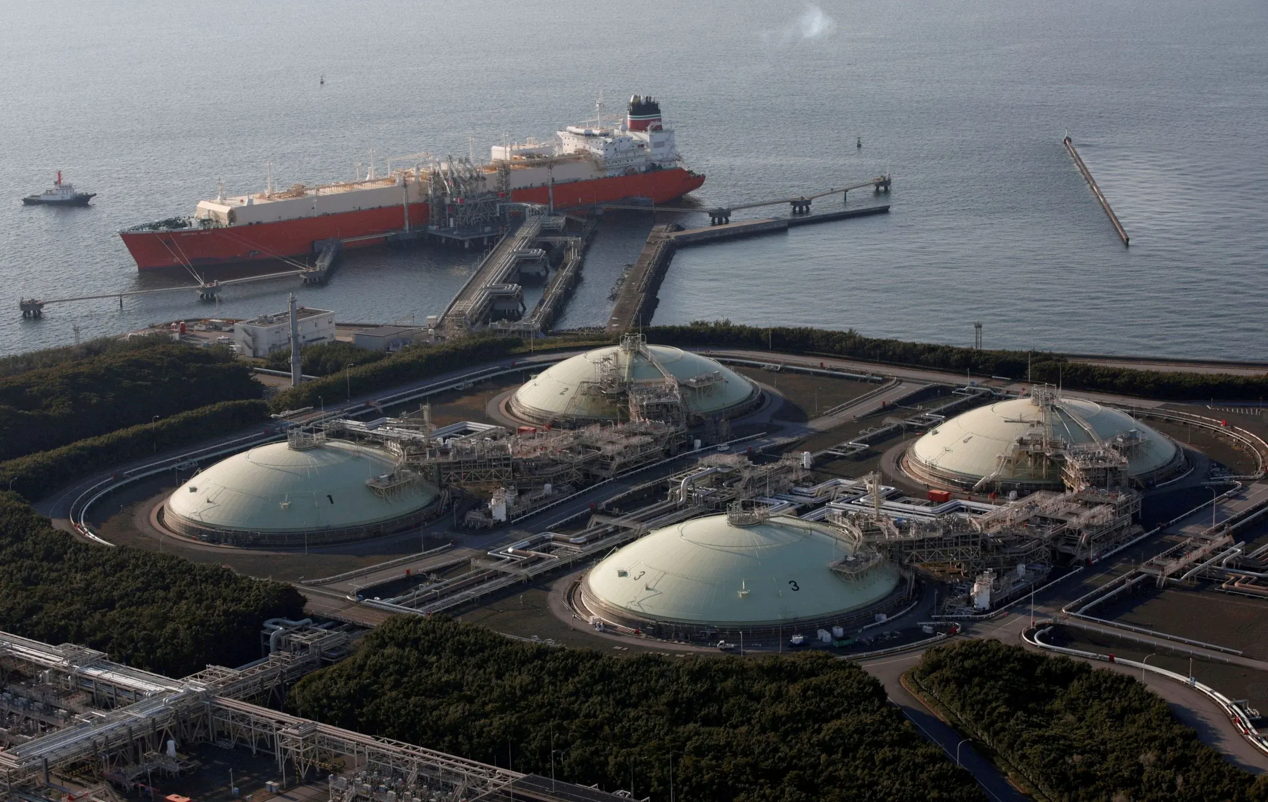 Aerial view of an LNG receiving terminal in Japan, with four domed storage tanks beside the sea and an LNG carrier moored at the jetty